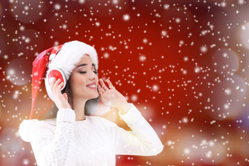 Young woman in Santa's hat with headphones listening to music and snow effect on color background. Christmas and New Year songs