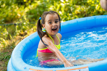 Little girl in an inflatable pool in the garden near the house