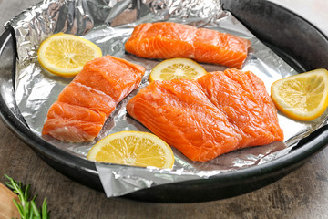 Frying pan with foil, slices of lemon and salmon, closeup