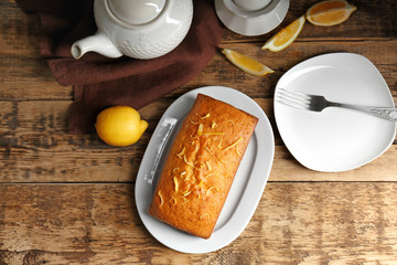 Plate with citrus cake and orange zest on wooden table