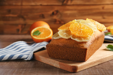 Cutting board with delicious citrus cake and sliced fruits on wooden table