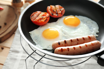 Frying pan with tasty eggs, sausages and tomatoes on table