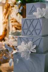 A classic tiered square grey cake with flowers decoration and geometric pattern.