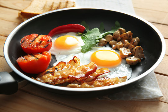 Frying pan with tasty eggs, bacon and tomatoes on table