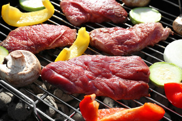 Raw tasty beefsteaks and vegetables cooking on barbecue grill, close up