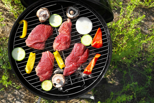 Raw tasty beefsteaks and vegetables cooking on barbecue grill outdoors