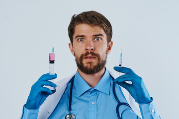 Man with a beard on a light background holds syringes in a medical gown, portrait, medicine, doctor