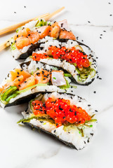 Trend hybrid food. Japanese Asian cuisine. Mini sushi-tacos, sandwiches with salmon, hayashi wakame, daikon, ginger, red caviar. White marble table, with chopsticks, soy sauce. Copy space