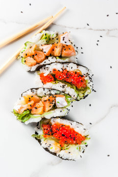 Trend hybrid food. Japanese Asian cuisine. Mini sushi-tacos, sandwiches with salmon, hayashi wakame, daikon, ginger, red caviar. White marble table, with chopsticks, soy sauce. Copy space top view