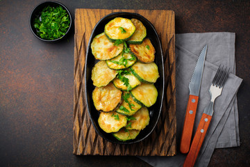 Fried zucchini with red hot pepper, basil and parsley in a cast-iron frying pan on  old dark background. Selective focus. Top view. Copy space.