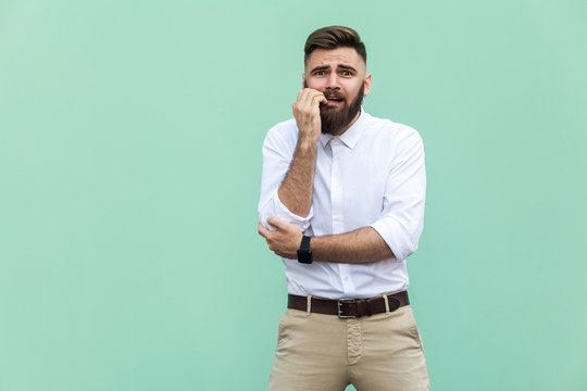 Stylish bearded businessman with warried. Hipster guy having shocked face, looking at camera. Indoor, studio shot, light green background
