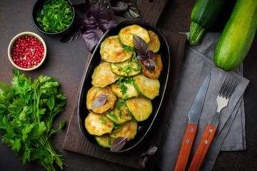 Fried zucchini with red hot pepper, basil and parsley in a cast-iron frying pan on  old dark background. Selective focus. Top view. Copy space.
