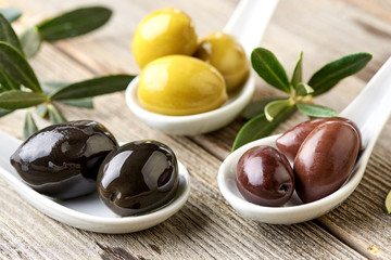 Different kind of olives green olives, black olives, kalamata olives and olive branch on wooden light table. Variations of olives.