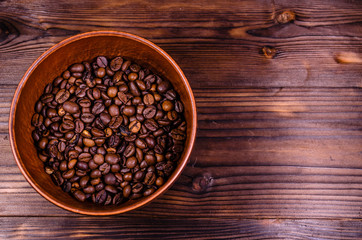 Roasted coffee beans in bowl on wooden table. Top view