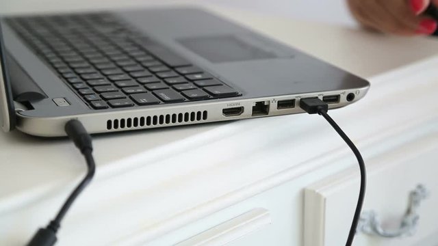Female hand inserting USB cable into laptop 