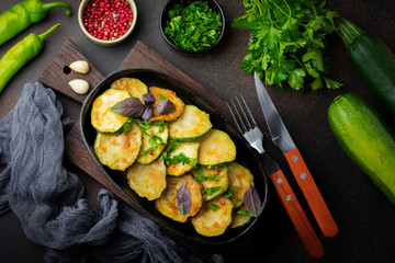 Fried zucchini with red hot pepper, basil and parsley in a cast-iron frying pan on  old dark background. Selective focus. Top view. Copy space.