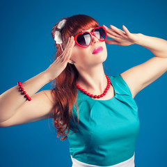 beautiful pin-up girl posing with red heart-shaped sunglasses against blue background
