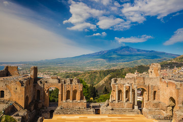 Panoramic view of beautiful town of Taormina with its greek amphitheatre and Etna volcano background, Sicily island, Italy - obrazy, fototapety, plakaty