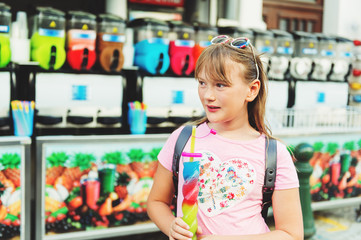 Cute little girl drinking colorful frozen slushie drink on hot summer day