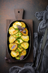 Fried zucchini with red hot pepper, basil and parsley in a cast-iron frying pan on  old dark background. Selective focus. Top view. Copy space.