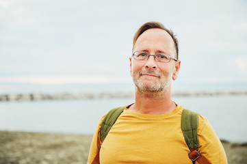 Handsome man on summer vacation by the sea, wearing yellow safran t-shirt and backpack