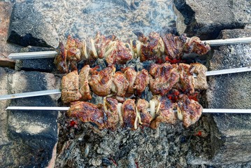 жареные куски мяса на шампурах над жаром от костра на...