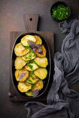 Fried zucchini with red hot pepper, basil and parsley in a cast-iron frying pan on  old dark background. Selective focus. Top view. Copy space.