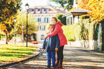 Big sister and small brother playing in autumn park, kids wearing bright warm jackets