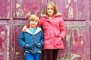 Obraz na płótnie Canvas Portrait of two adorable kids outdoors, wearing warm coats standing next to old purple background