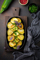 Fried zucchini with red hot pepper, basil and parsley in a cast-iron frying pan on  old dark background. Selective focus. Top view. Copy space.