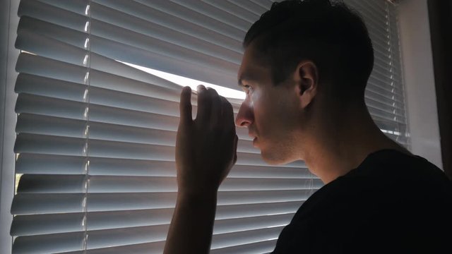 man looking out the window through the blinds to the street, spying. suspected