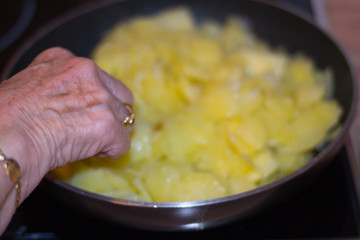 Old woman cooking traditional Spanish omelette. Cooking potatoes in a pan. Old doman hand. Traditional food concept.