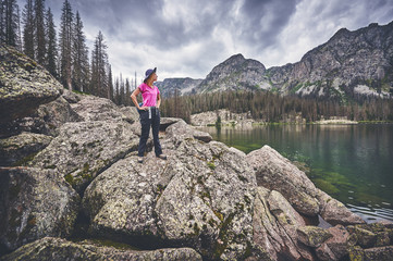 a young woman standing on boulders next to a mountain lake