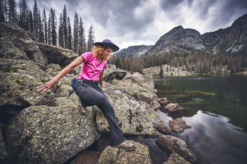 Fototapeta premium a young woman climbing on boulders next to a mountain lake