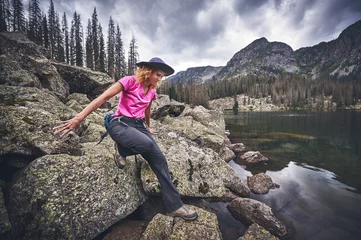 Fototapeten a young woman climbing on boulders next to a mountain lake © goodmanphoto