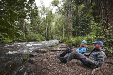 a man and woman sitting next to a mountain river