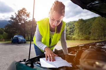 Woman reading a manual trying to fix the broken car