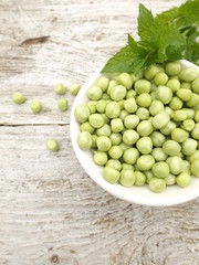 Peeled young green peas in a bowl and a bunch of mint