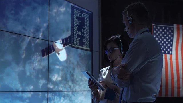 Side view of man and woman communicating in space flight control center. Some elements of this image furnished by NASA.