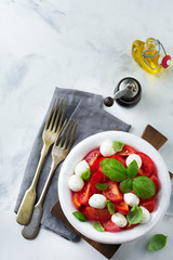 Traditional Italian caprese salad with tomatoes, mozzarella cheese and basil on a light marble background in a white old ceramic plate. Selective focus.Top view. Copy space.