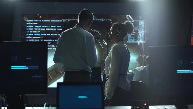 Side view of multiracial man and woman communicating in space flight control center.