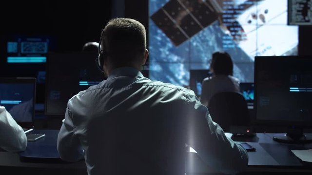 Movement shot back view of man working on space mission in control center. Observing the flight of a satellite in orbit. Elements of this image furnished by NASA.
