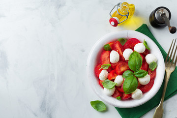 Traditional Italian caprese salad with tomatoes, mozzarella cheese and basil on a light marble background in a white old ceramic plate. Selective focus.Top view. Copy space.
