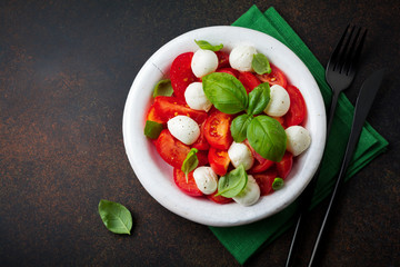 Traditional Italian caprese salad with tomatoes, mozzarella cheese and basil on  dark background in  white old ceramic plate. Selective focus.Top view. Copy space.