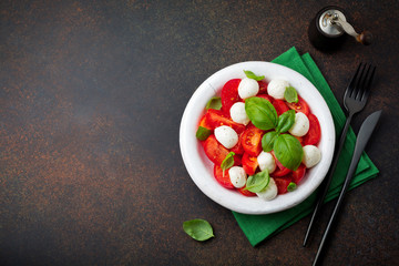 Traditional Italian caprese salad with tomatoes, mozzarella cheese and basil on  dark background in  white old ceramic plate. Selective focus.Top view. Copy space.