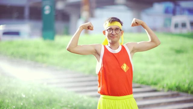 Funny guy freak smiling showing muscles in hands after workout in park.