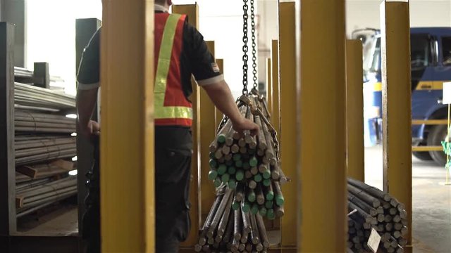 Factory Worker Helping Crane To Carry A Bundle Of Steel Bars 