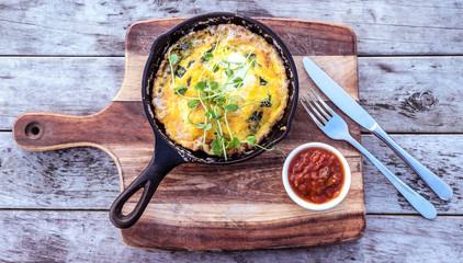 Egg omelette in cast iron skillet on wooden chopping board and rustic timber background