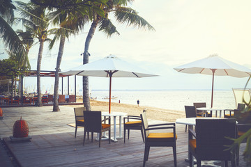 Cafe and restaurant chairs with table and umbrella at beach. Famous travel destination in Sanur, Bali, Indonesia.