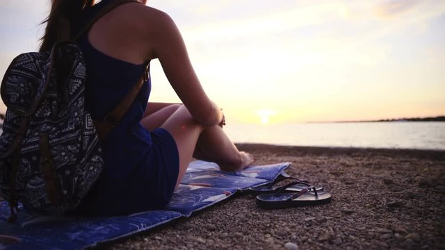 Woman sit on underlay at beach with flipflops beside 4K